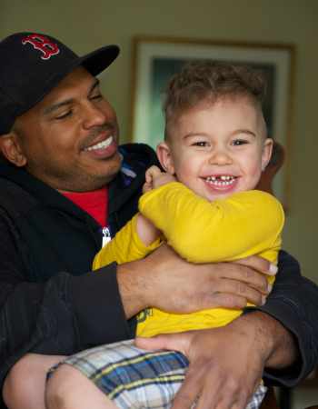 Father wearing baseball cap holding smiling young boy in his arms