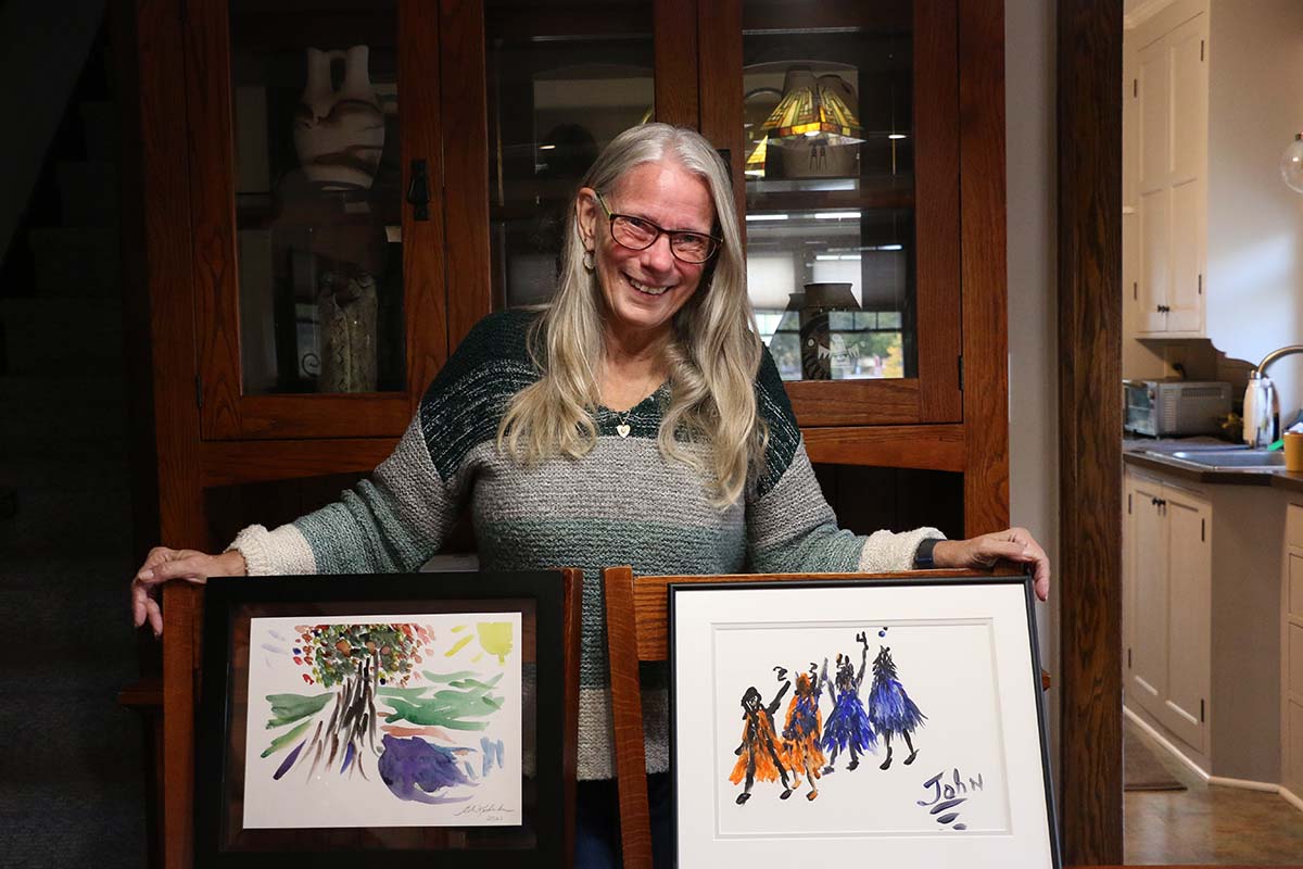 Chris Kuderka stands in front of two framed pictures painted by her husband at Wilder Connect