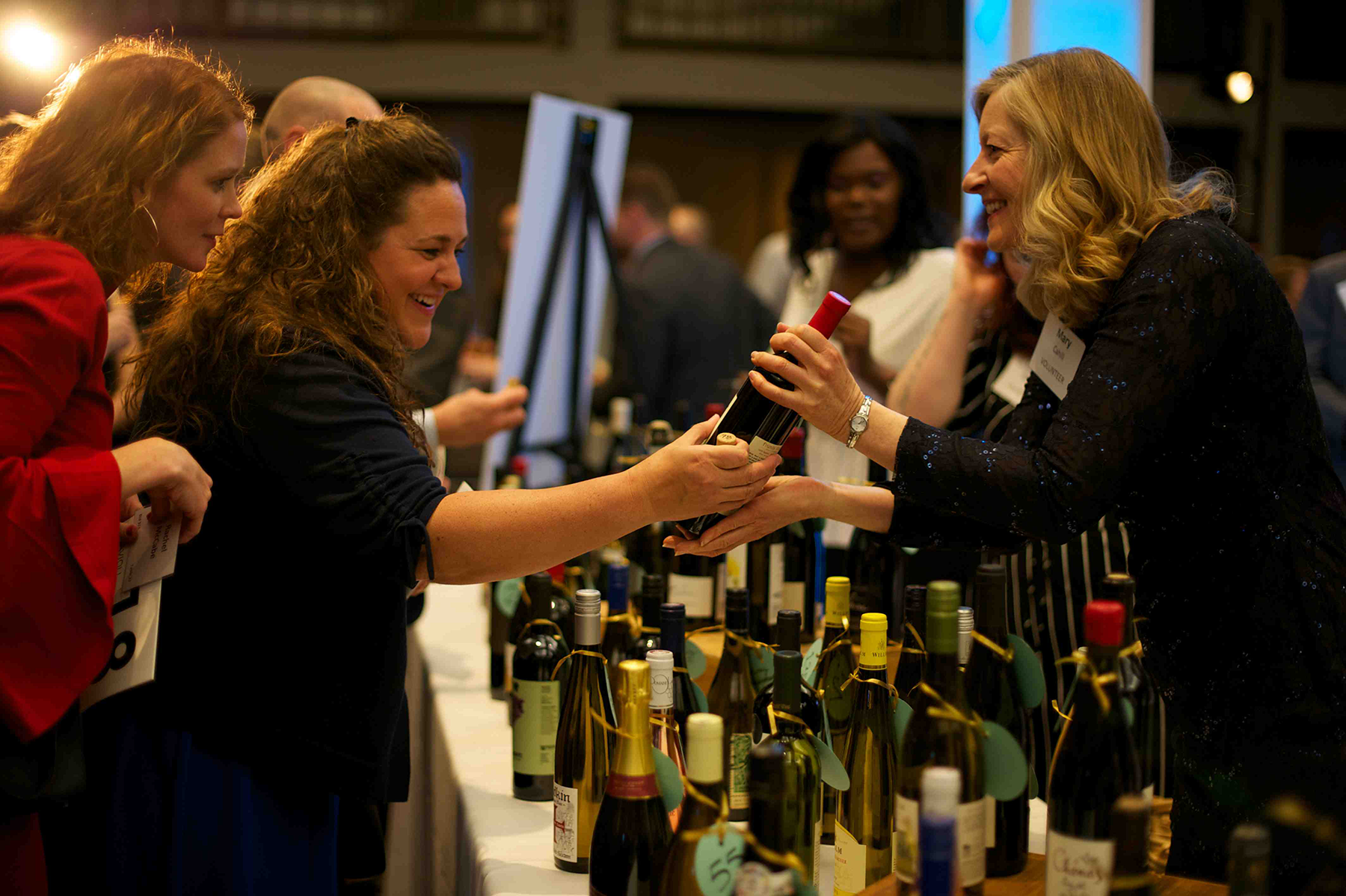 A guest at Ordinary Magic accepts a wine bottle from volunteer Mary Cahill at the event's wine-pull fundraiser