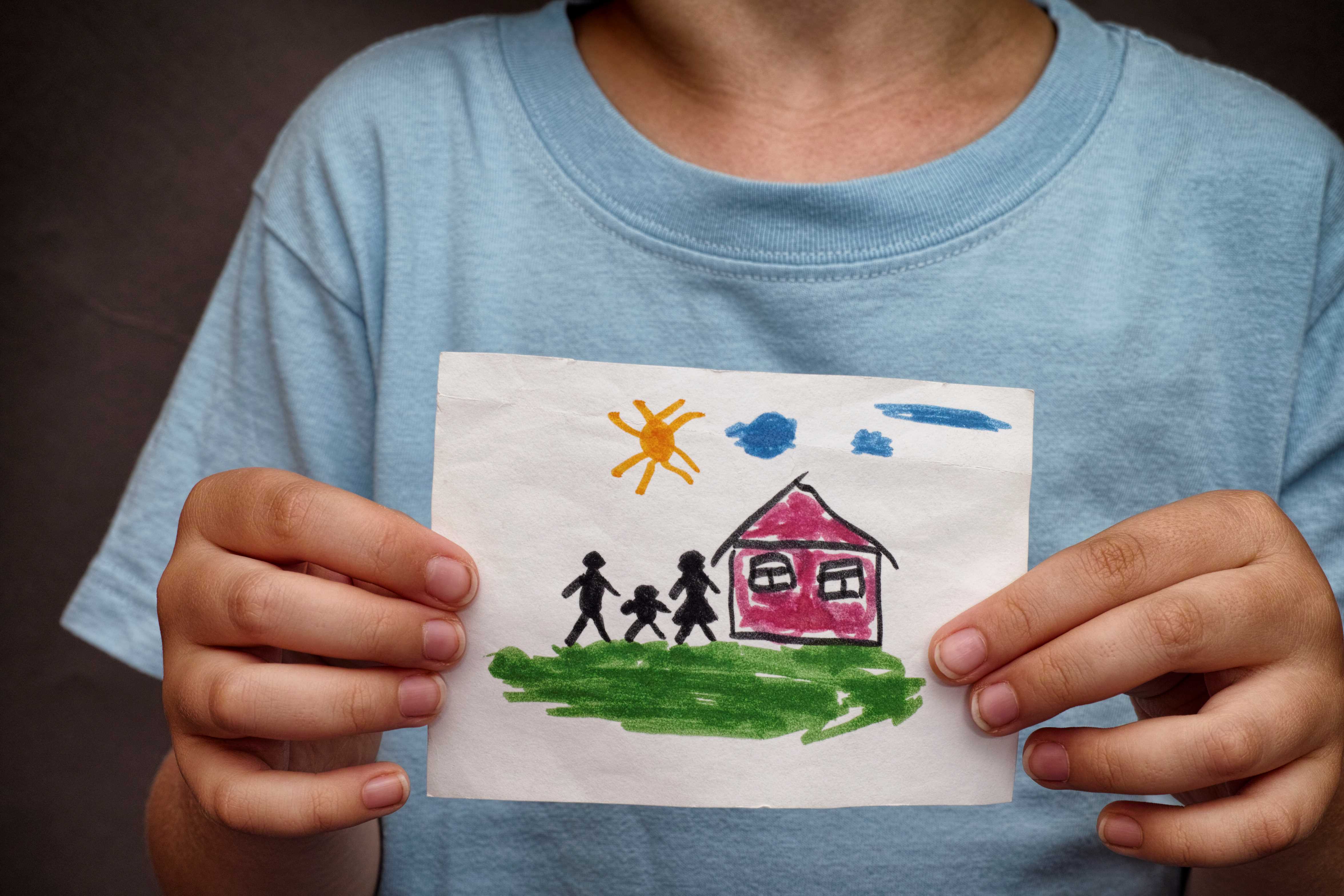 Child holding painting of home in front of them