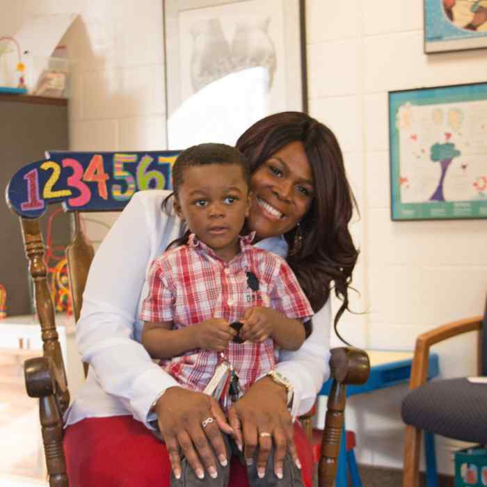 child sitting in parent's lap, black mother and child, child development center family, child at preschool with mother