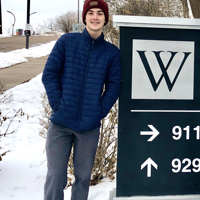 Male high school student in winter clothes leaning against a sign
