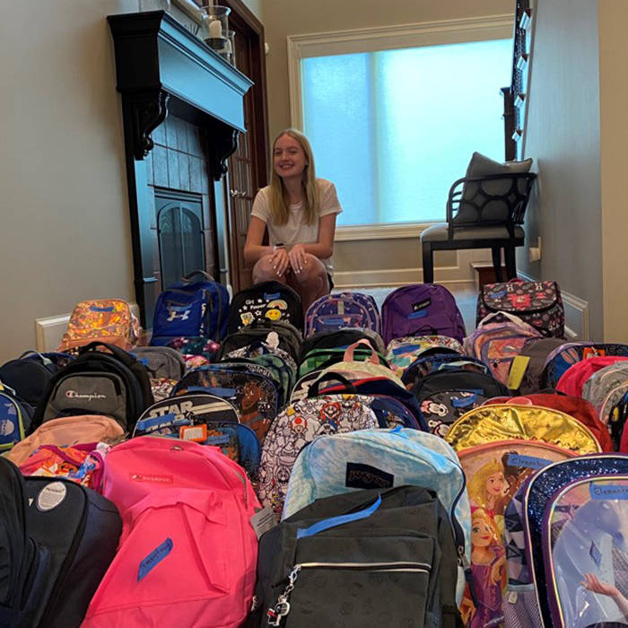 Girl posting behind backpacks donated to Wilder's annual backpack drive