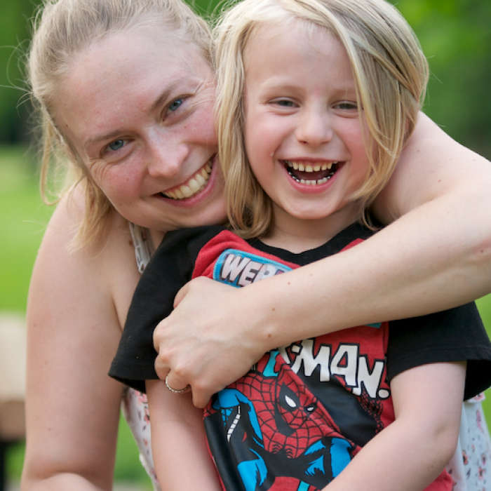 Photo of a mom hugging child, both smiling and looking at the camera