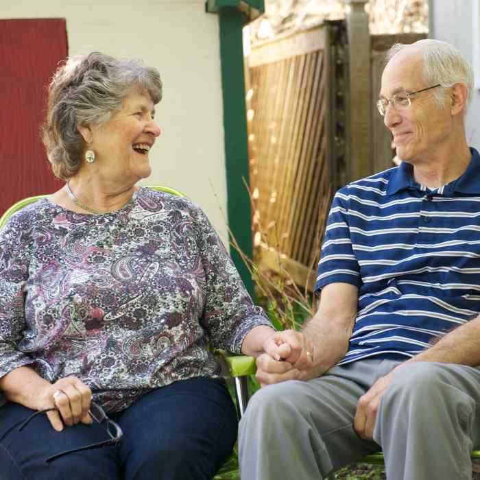Older man and woman sitting next to each other outside and holding hands