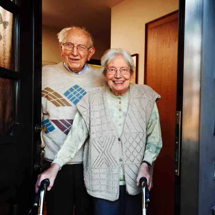 Older man standing behind woman with walker in doorway 