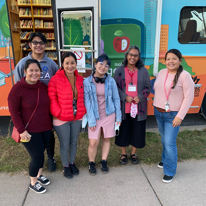 Six people stand in a row in front of a bookmobile entrance. 
