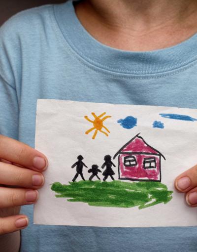 Child holding painting of home in front of them