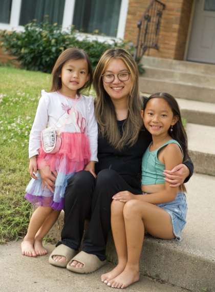 woman and two girls sitting together with house in the background
