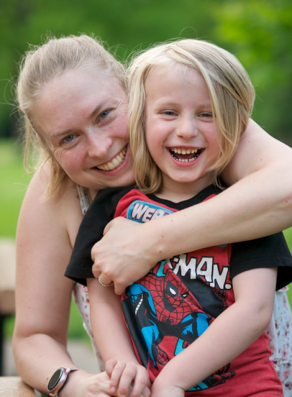 Photo of a mom hugging child, both smiling and looking at the camera