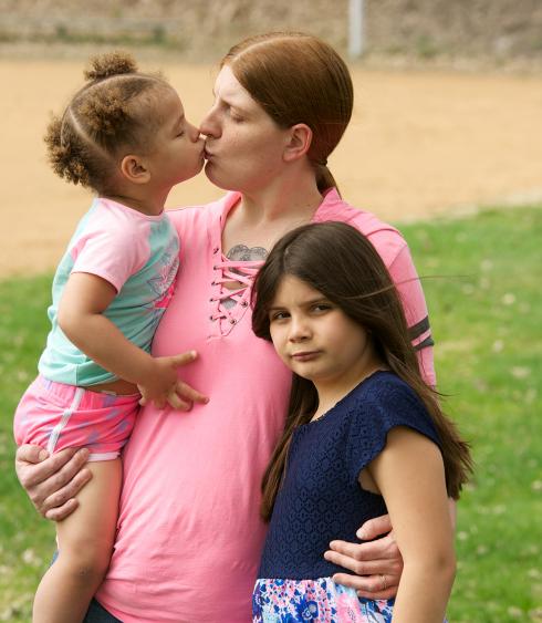 A woman kisses a toddler and holds a child.