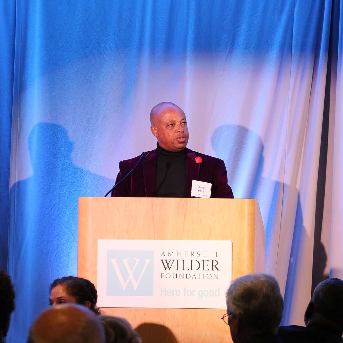 Kevin Harris speaking at the podium at Ordinary Magic, Wilder's signature fundraising event
