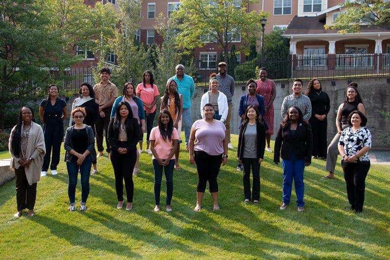 A photo of 22 people standing outdoors in a grassy area in three rows. They are smiling and facing the camera.