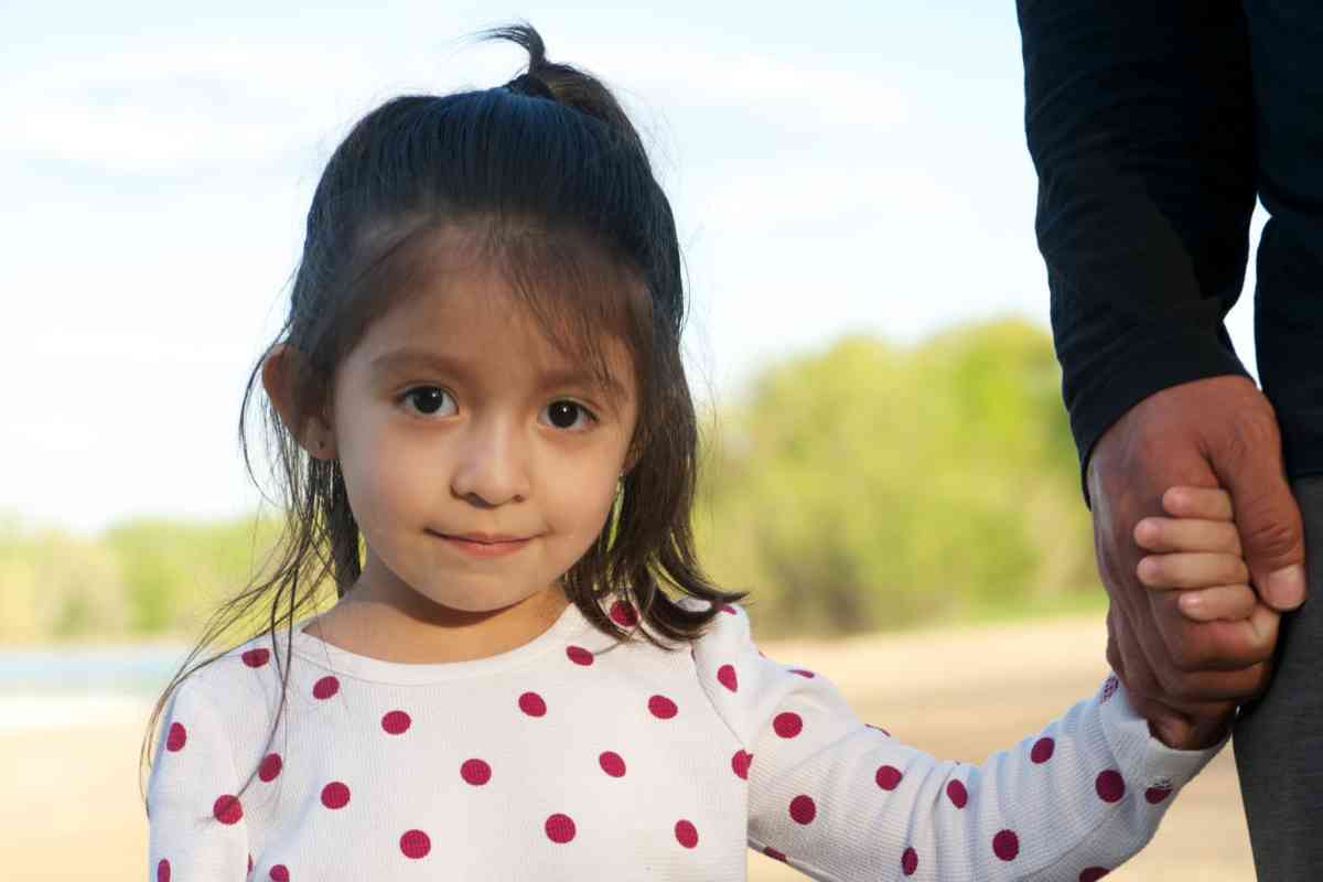 girl looking at camera, holding hands with adult