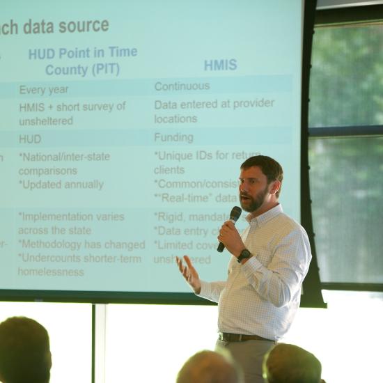 Male researcher speaking with microphone in front of projector screen