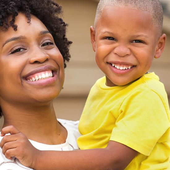 A woman holds a child in her arms and they both smile into the camera.  