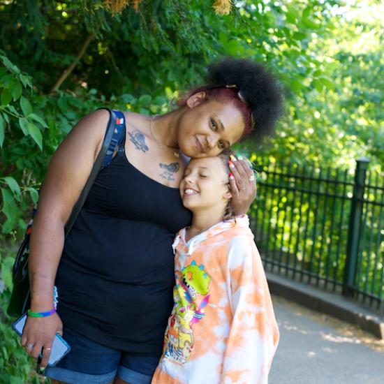 Young woman standing next to child with arm around their shoulder