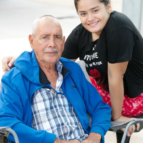 Older man sitting in chair with young woman standing behind