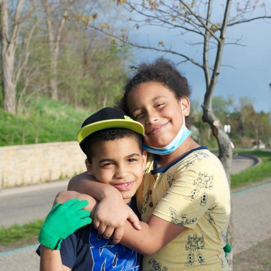 Two children with arms around their shoulders and smiling 
