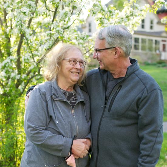 A married elderly couple side hugging and looking at each other while they're outside during the spring time.