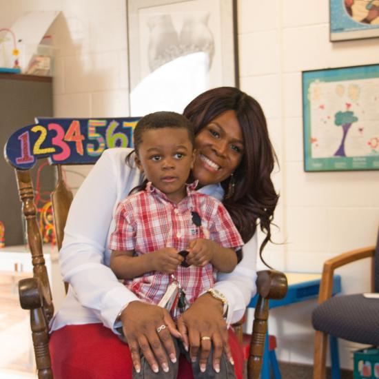 child sitting in parent's lap, black mother and child, child development center family, child at preschool with mother