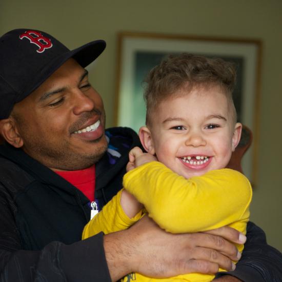 Father wearing baseball cap holding smiling young boy in his arms