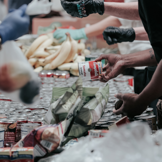 People collect fresh fruit and canned goods from a long table. 