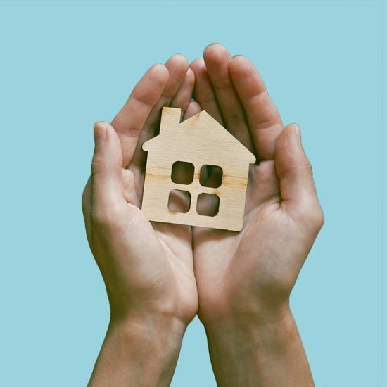 A pair of hands hold a small cutout of a wood house.