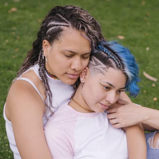 Two people sit on the grass arm in arm.