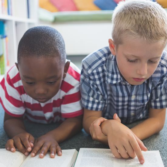 Two young children read books on the floor of a library.