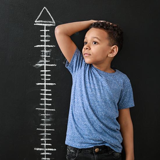 A boy stands next to wall chart measuring height.
