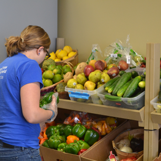 A woman faces and selects from shelves of fruit and vegetables.
