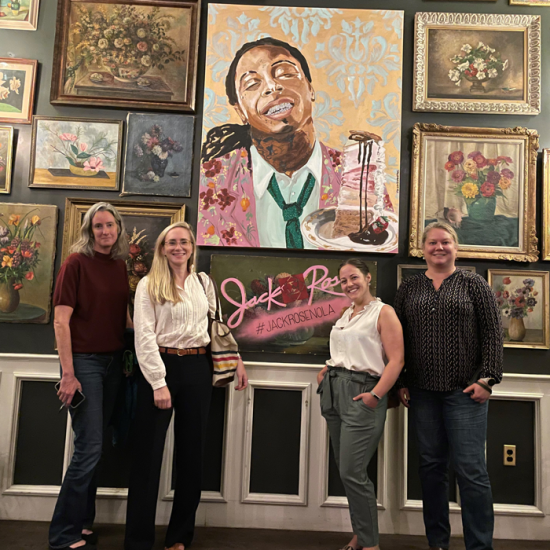Four women stand in front of a wall of paintings in a New Orleans restaurant.