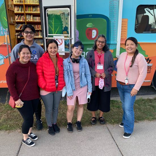 Six people stand in a row in front of a bookmobile entrance. 