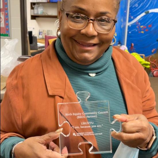 Sameerah Bilal-Roby holding glass, puzzle-shaped community partner award from the Birth Equity Community Council