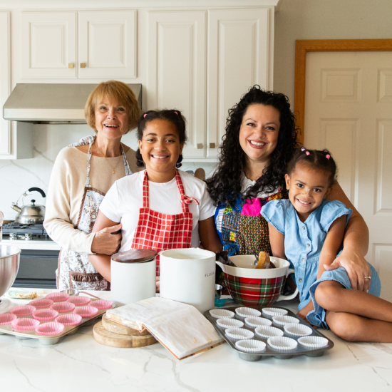 A multi-generational family stands at a kitchen counter, surrounded by baking materials.