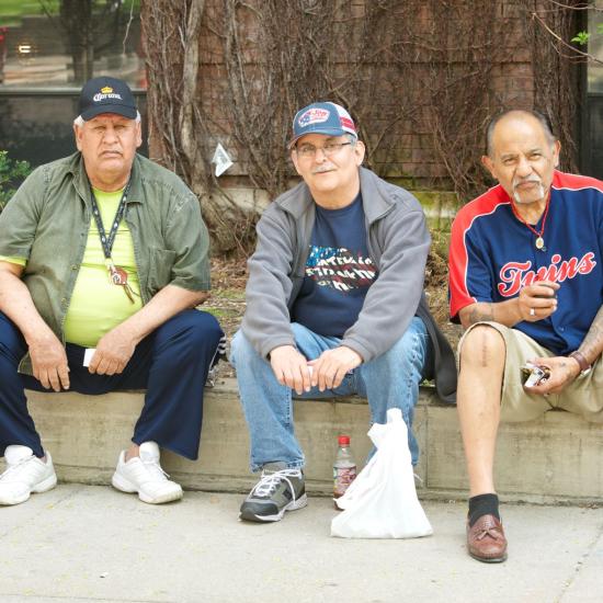 Three older men sitting on a wall.