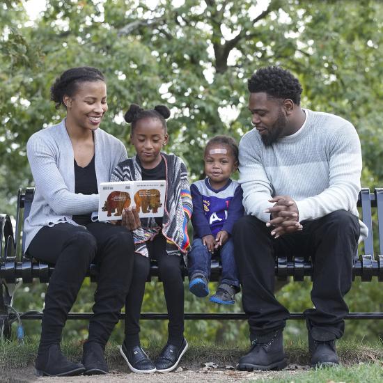 African American family sitting on park bench, african american mother and father with daughter and son, child development center family, minnesota community childcare, preschool family in saint paul minnesota