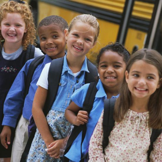 School children wearing backpacks stand outside a bus