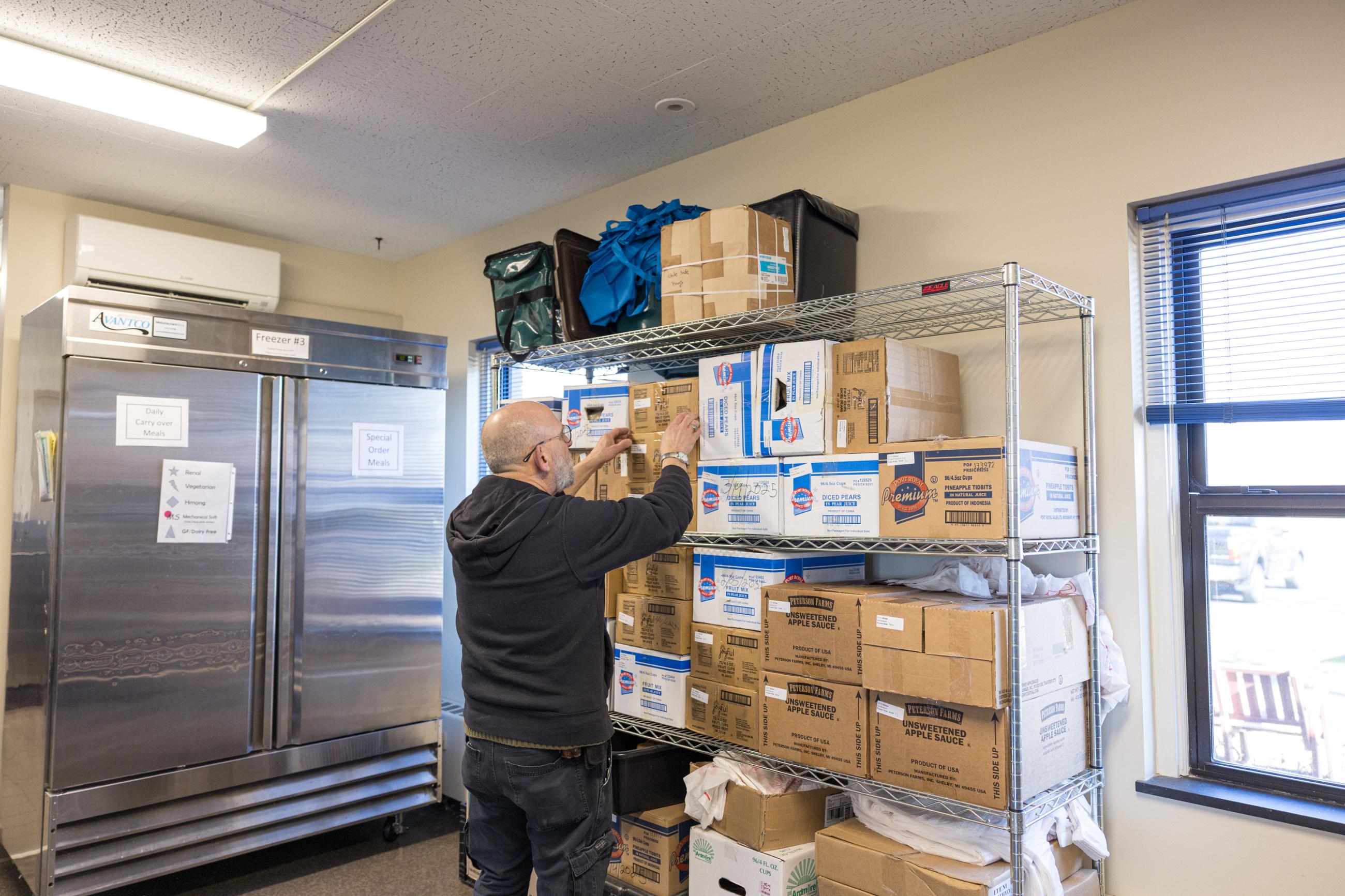 Meals on Wheels volunteer grabbing supplies from a storage rack.