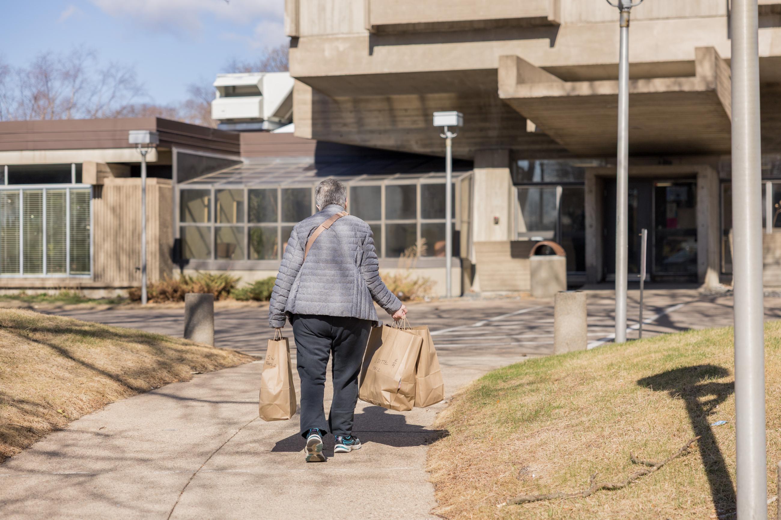Volunteer carrying three meal bags walking towards hi-rise apartments.