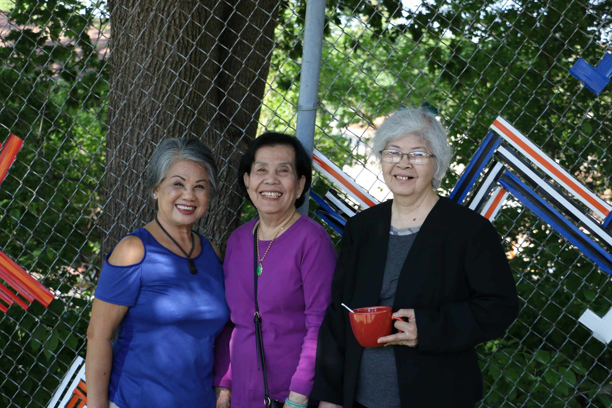 Three women pose by new fence weaving outside Wilder Center for Social Healing