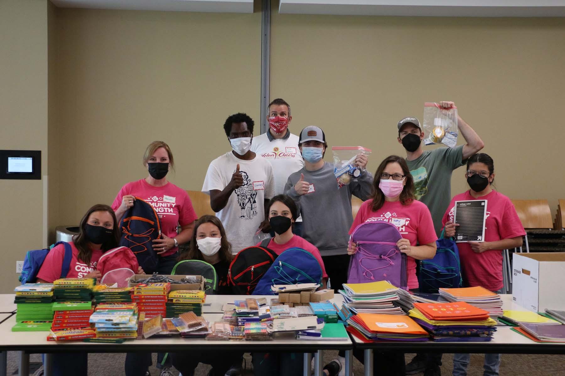 A group of people standing behind a table with school supplies holding up school supplies