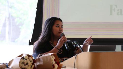 Woman with dark hair speaking behind a podium with a screen behind her