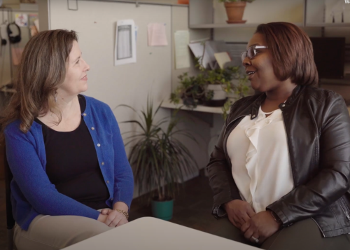 Two women sit at a table and look at each other while engaged in conversation