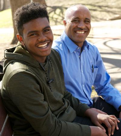 Son and father sitting on a park bench smiling