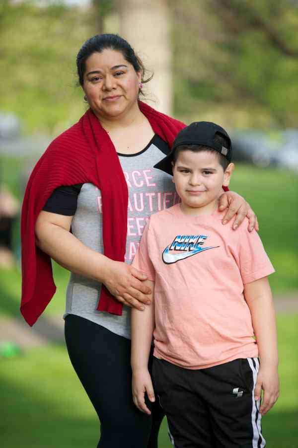 Woman with hands on shoulders of boy, both smiling and posing