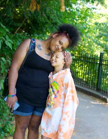 Young woman standing next to child with arm around their shoulder
