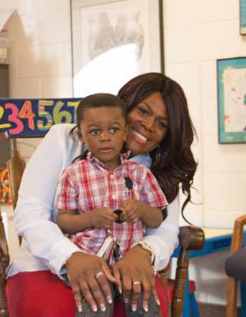 child sitting in parent's lap, black mother and child, child development center family, child at preschool with mother