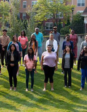 A photo of 22 people standing outdoors in a grassy area in three rows. They are smiling and facing the camera.
